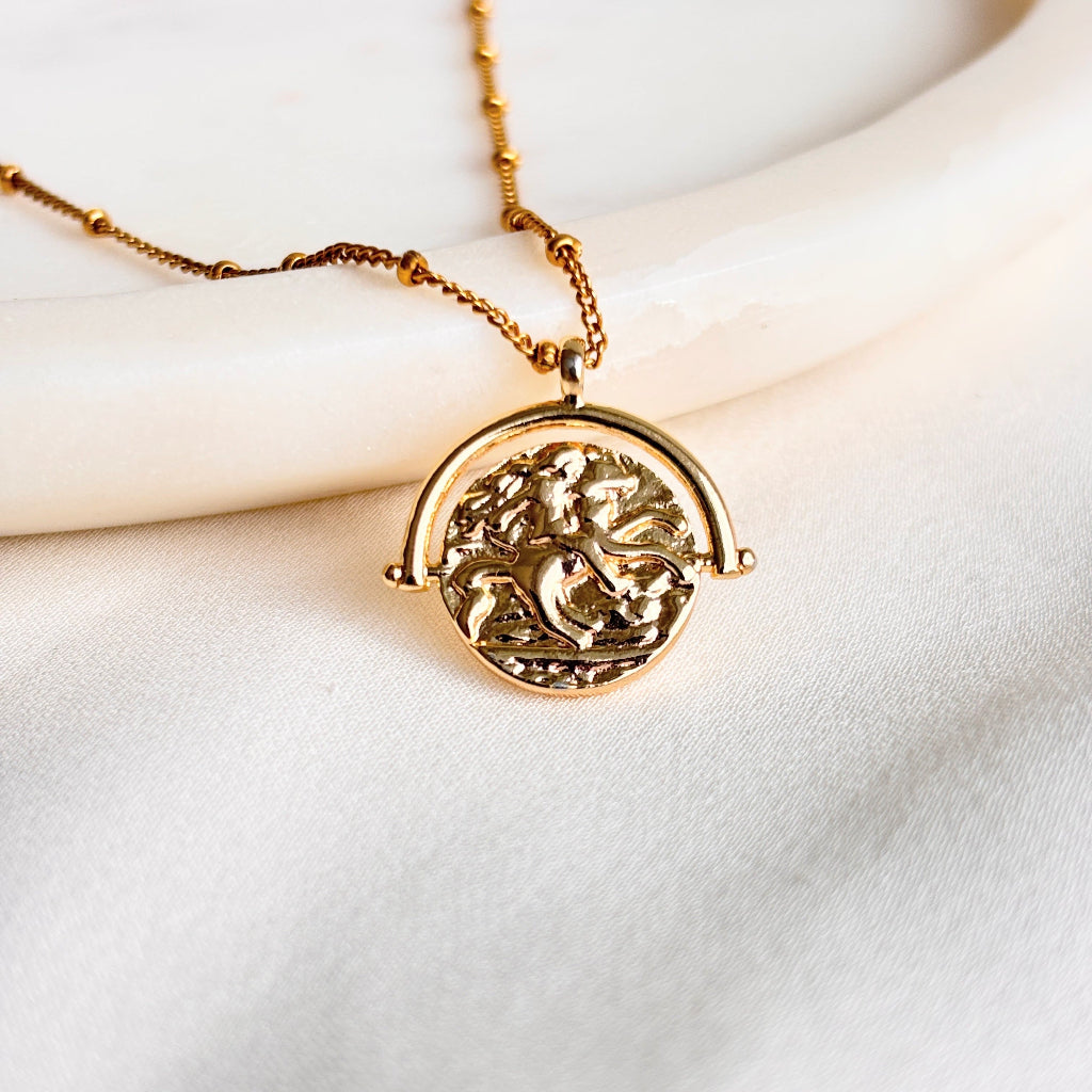 a vintage inspired coin pendant necklace on 14k gold filled beaded chain. The faux spinner coin depicts Lady Godiva riding on horseback.