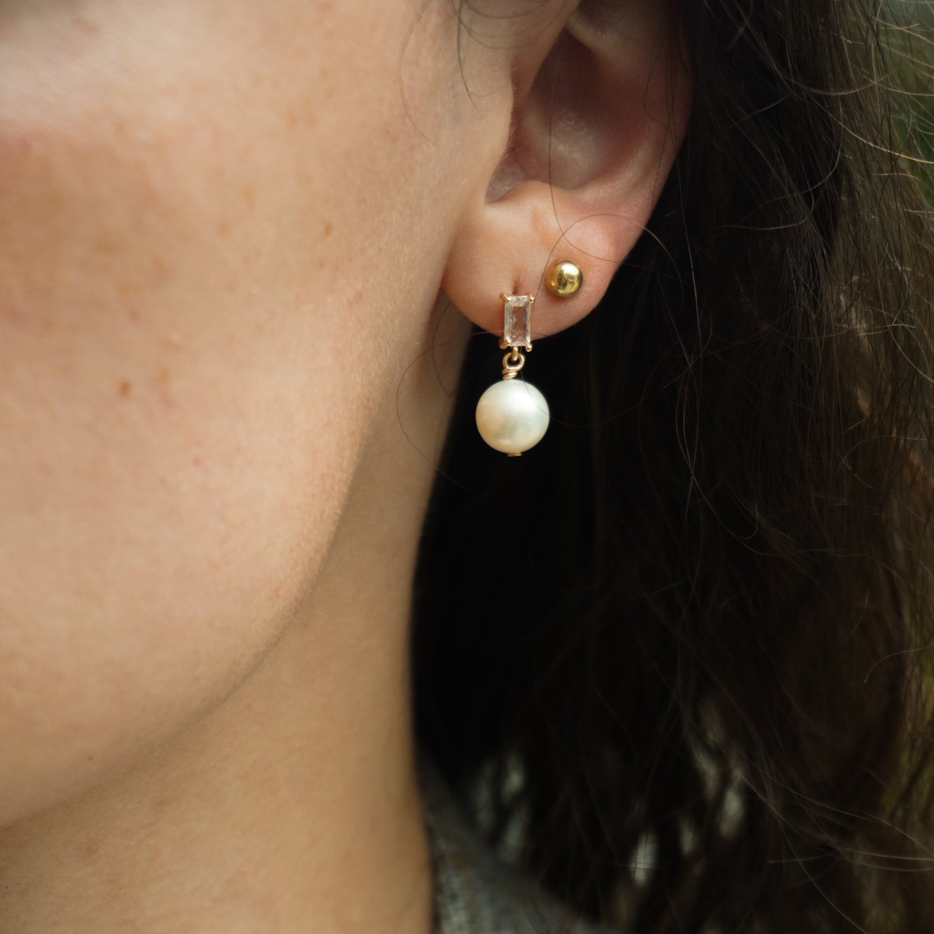 close-up of a cubic zirconia baguette post earring with a dangling 8mm pearl shown on ear lobe.