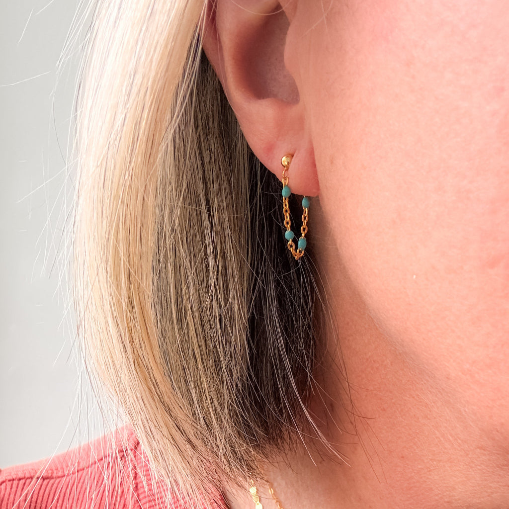 a dainty 14k gold filled wrap around hoop earring that features dainty turquoise beaded chain that dangles from a gold sphere post earring shown on lobe