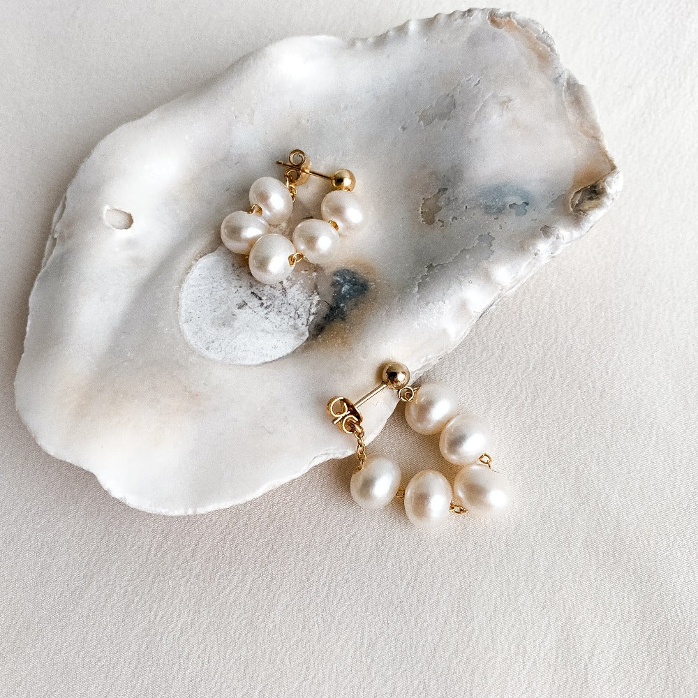 Dainty natural pearl earrings featuring 5 oval freshwater pearls strung on chain in a wrap around design to form a hoop that dangles from gold ball stud earrings.