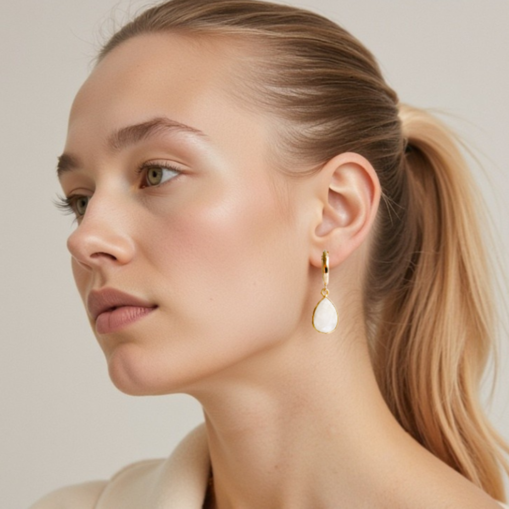 14k-gold filled bezel teardrop-shaped moonstone pendant hoop earrings shown on lobe of AI generated image of a woman to show approximate size of the earrings.