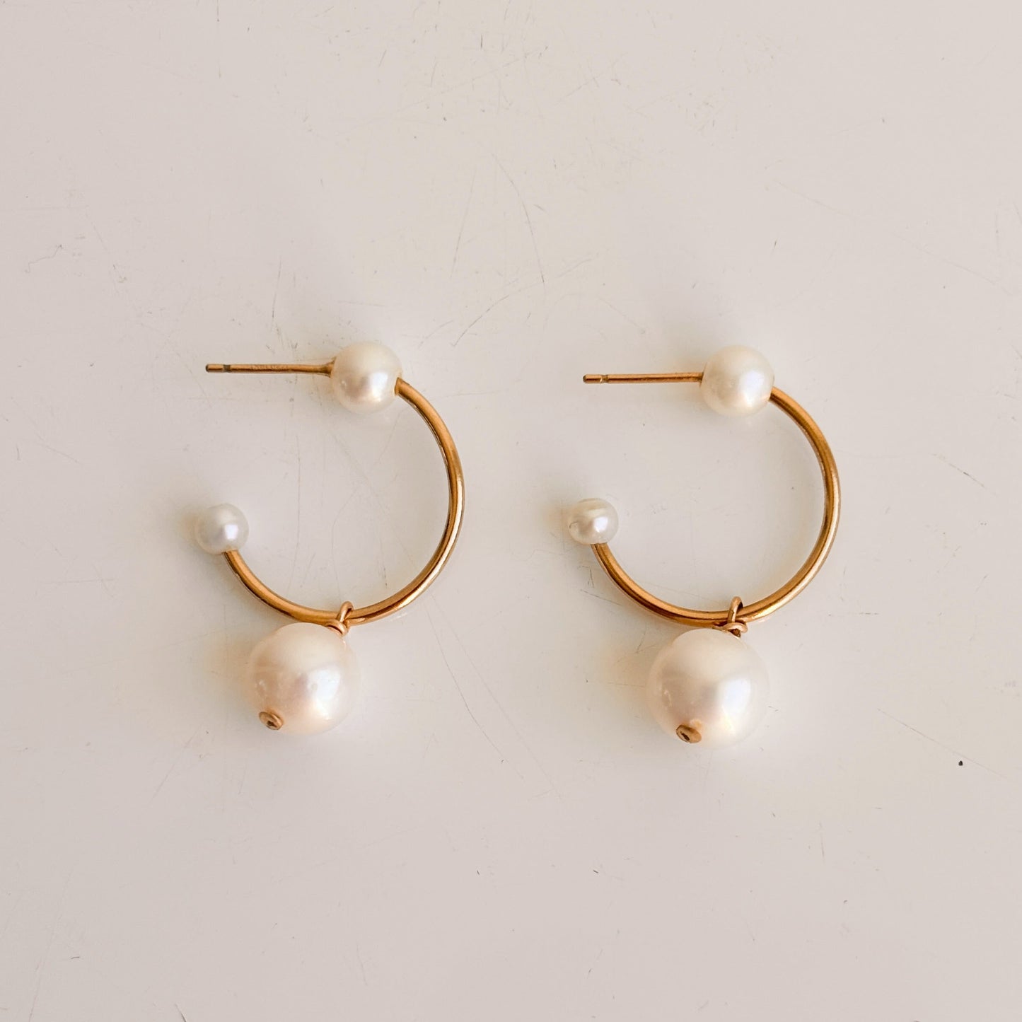 Pair of gold hoop earrings with pearl beads on a light gray background