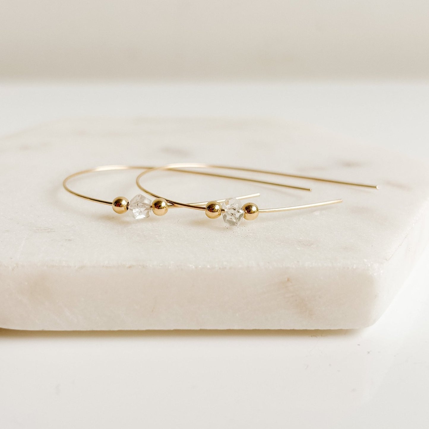 a pair of 14k gold filled wire pull through earrings featuring a tiny double pointed Herkimer Diamond crystal accented with a tiny gold sphere above and below it. The gemstone is threaded onto the wire.