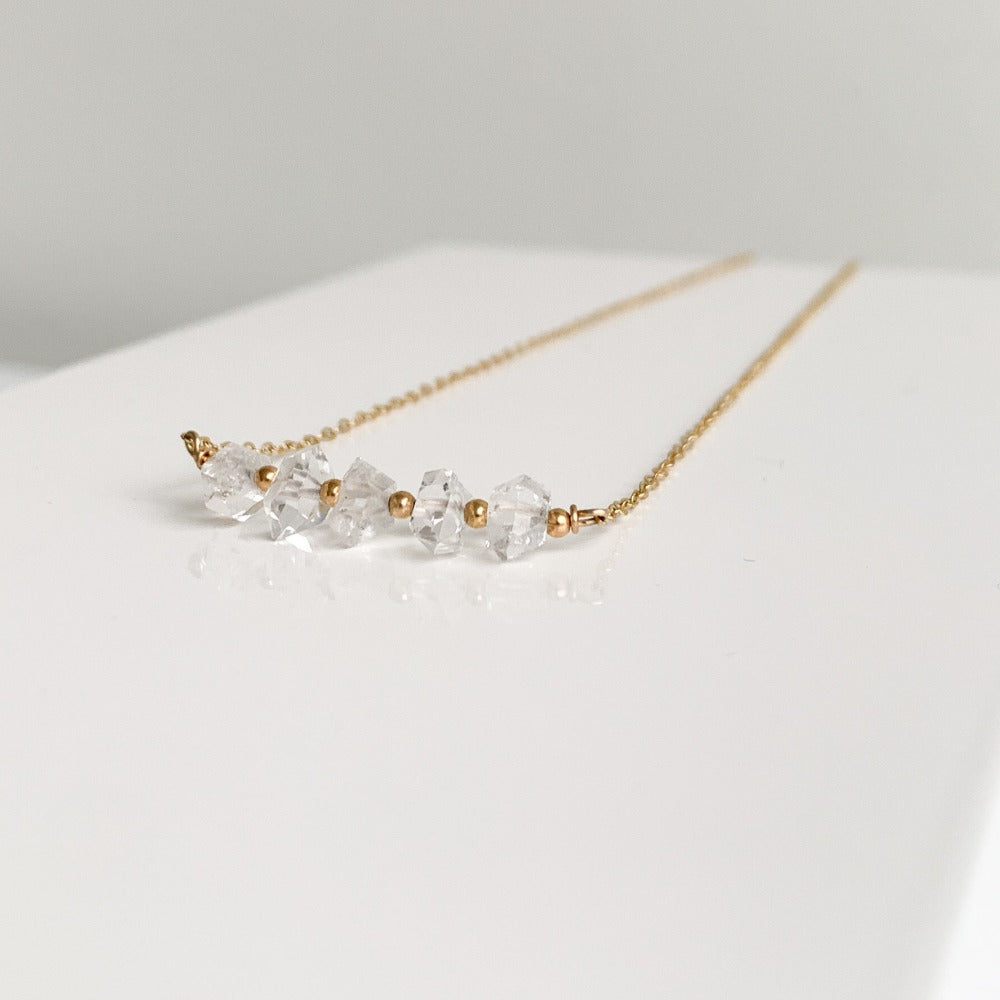 a dainty 14k gold filled necklace showcasing a row of herkimer diamond crystals alternating with tiny gold beads set in delicate chain.