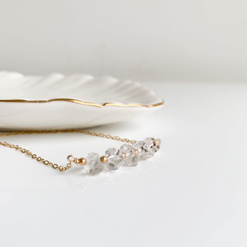 A dainty necklace with a horizontal bar of five double pointed clear crystal Herkimer Diamonds embellished with tiny gold beads on a delicate chain.