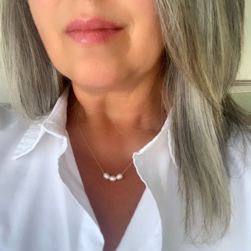 A dainty pearl necklace shown on neck. The simple gold chain necklace features three oval pearls that are strung on the chain.