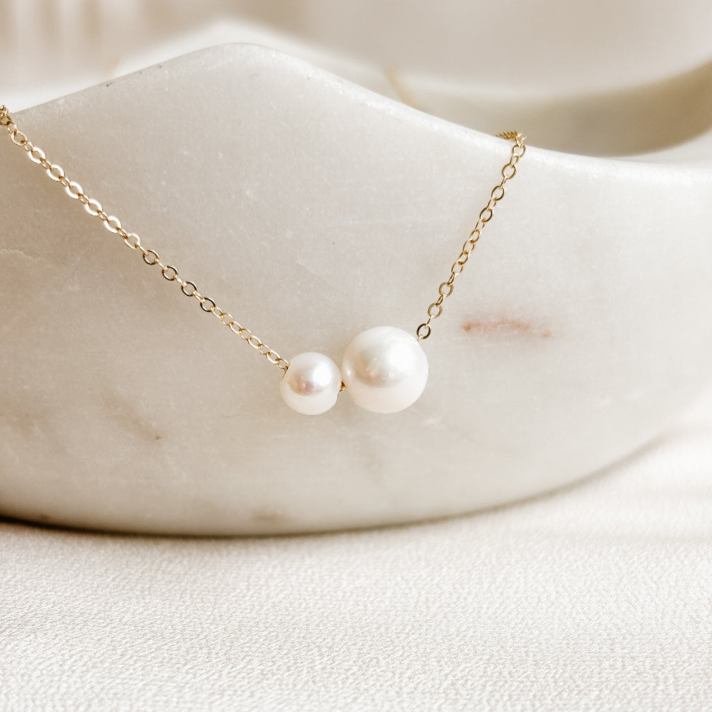 Double pearl necklace with 14k gold filled chain on a marble surface. The freshwater pearls are slightly different sizes and represent marriage, best friend, mother daughter relationship.