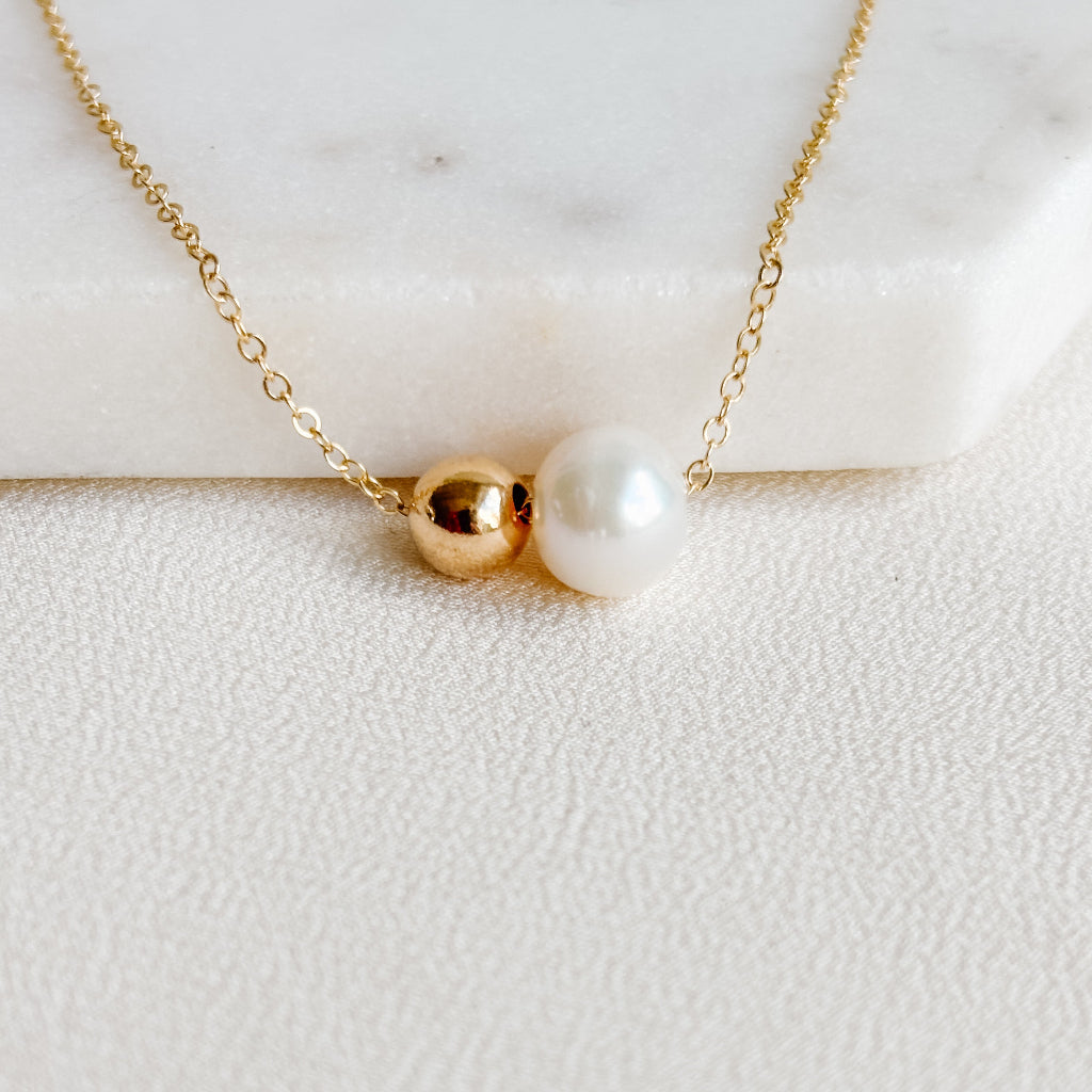 Gold necklace with a gold bead and pearl on a white marble surface