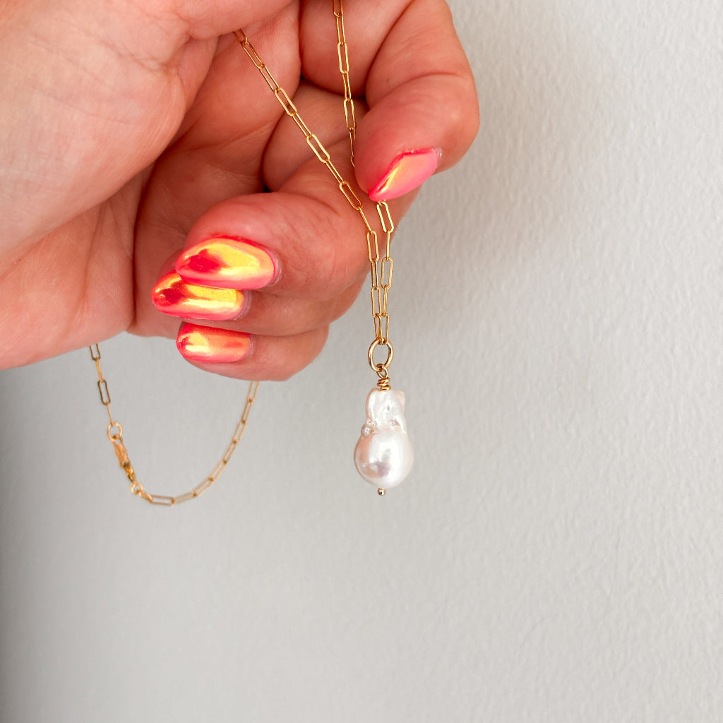paperclip chain necklace featuring a large natural fireball pearl pendant shown dangling from a woman's hand.