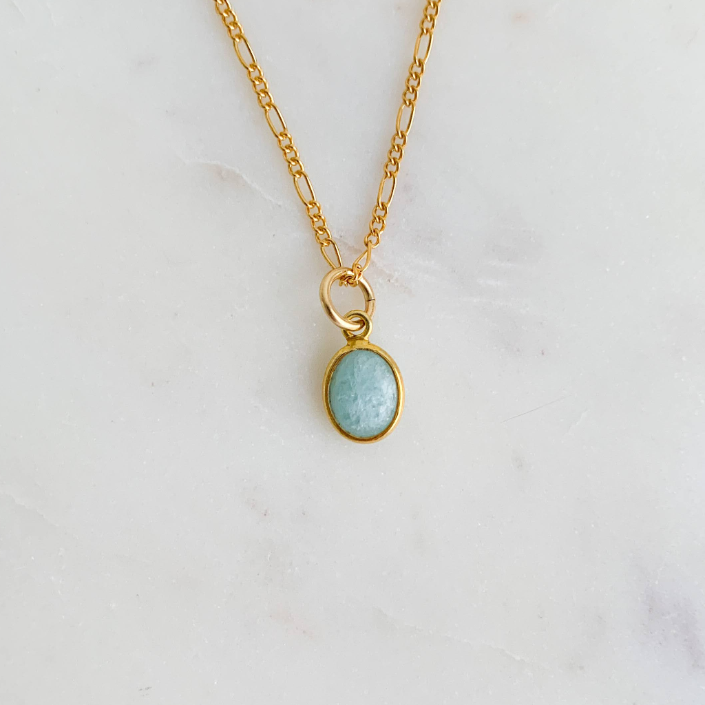 a single bezel set oval gemstone charm featuring smooth natural aquamarine is shown as a pendant on a necklace chain.