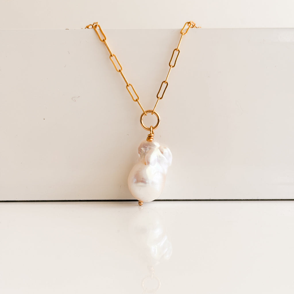 14k gold filled paperclip chain necklace with central ring from which dangles a large baroque fireball pearl drop.