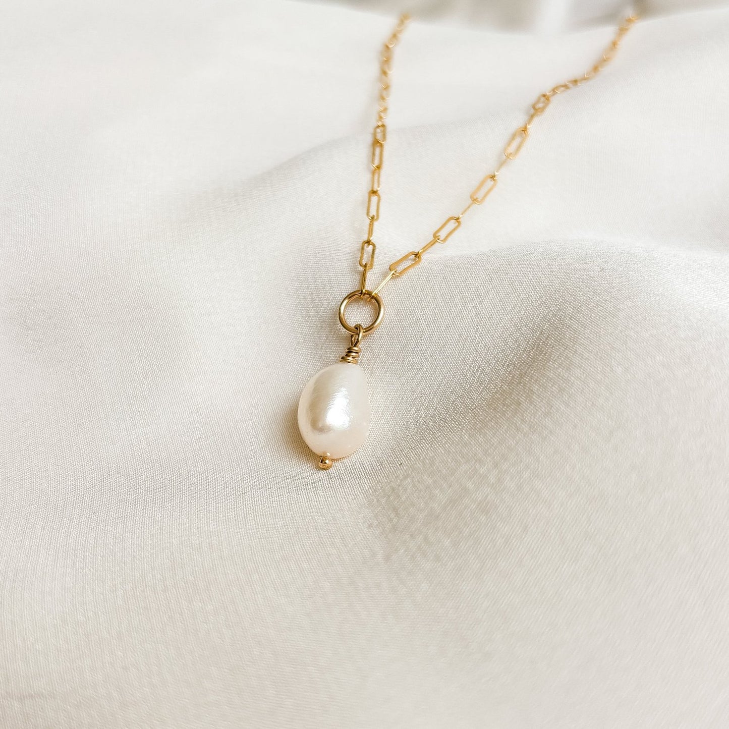 dainty paperclip necklace featuring a single white oval shaped pearl that dangles from a central ring.