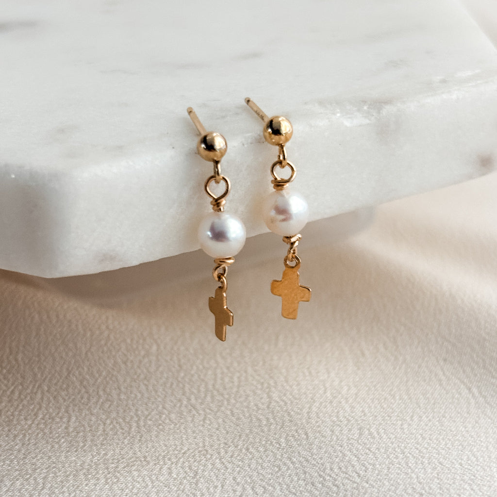 14k gold filled ball post earrings with dangling pearls and crosses on a marble surface