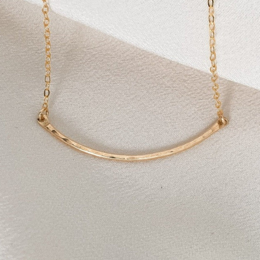 dainty gold necklace featuring a hammered curved bar set in the chain.