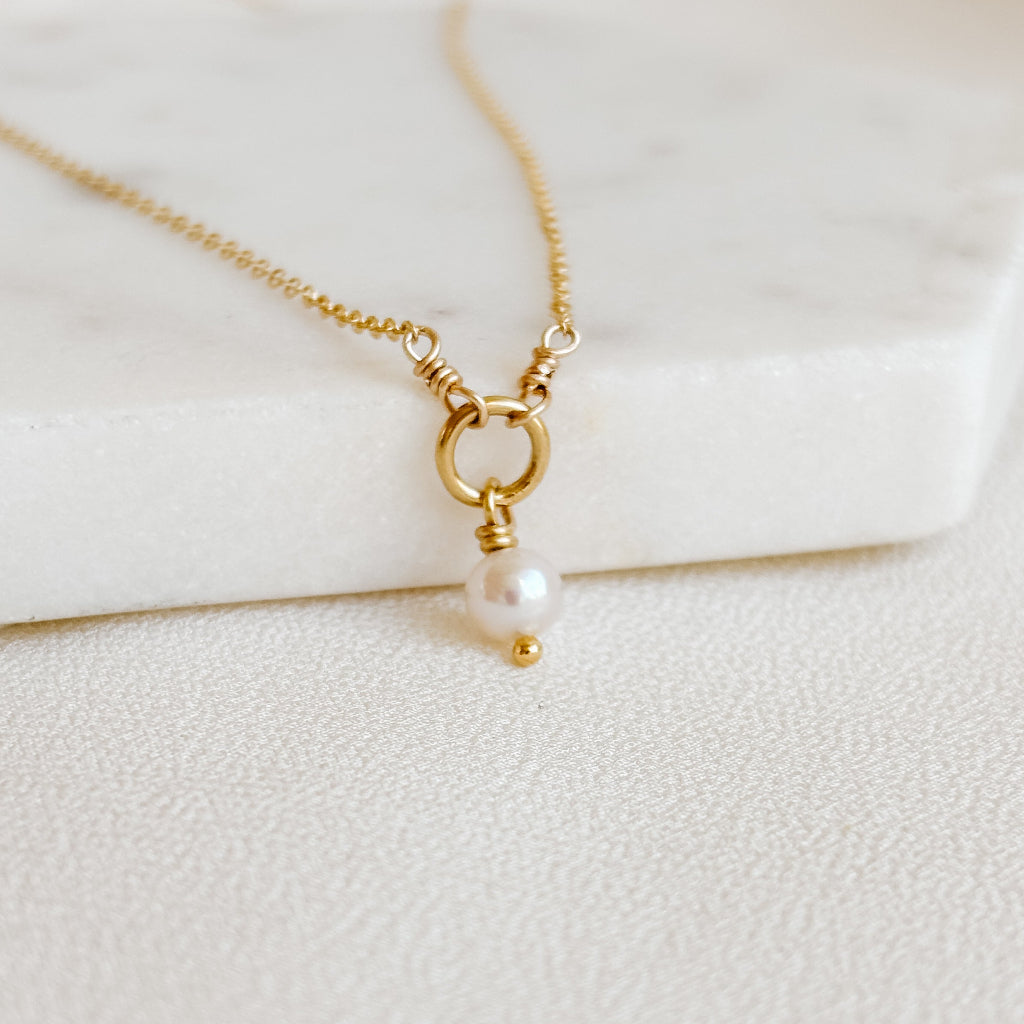 Gold necklace with a single pearl pendant on a light background