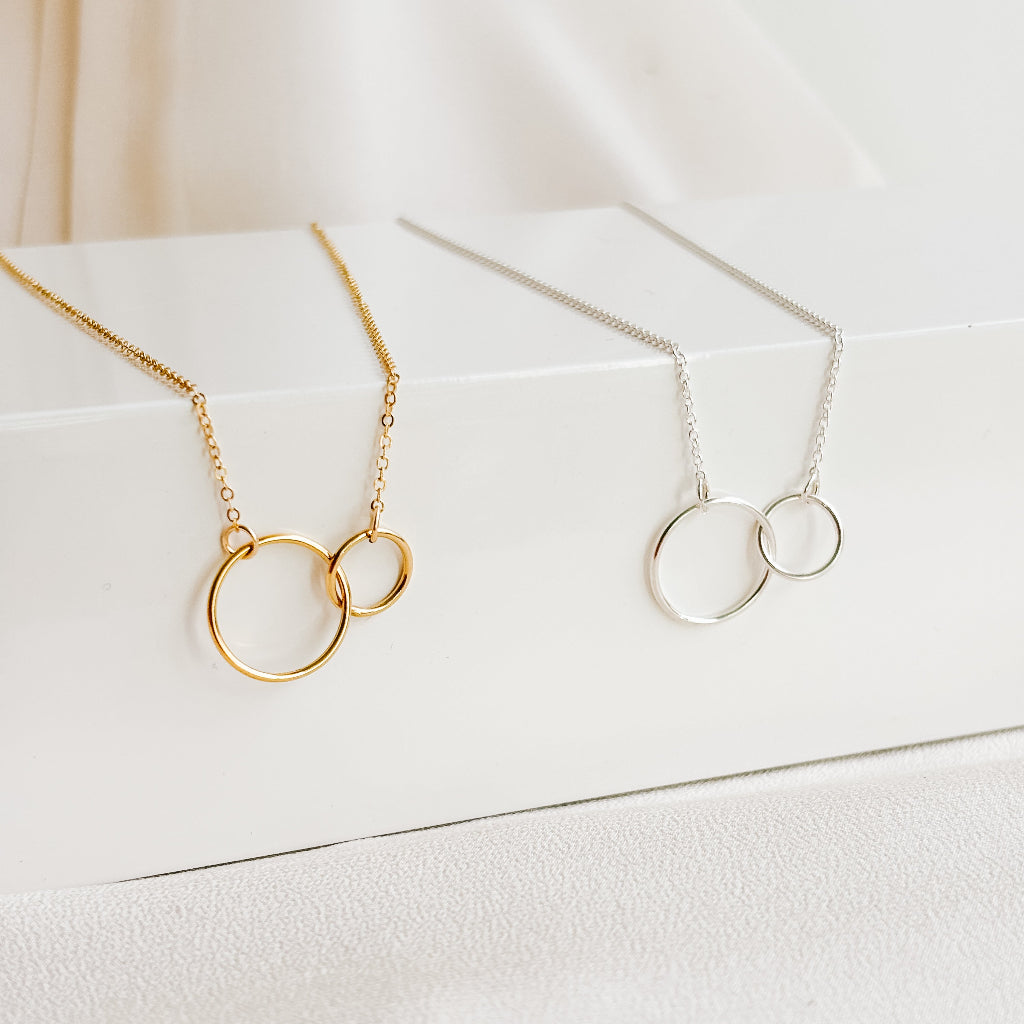 Two necklaces with interlocking rings on a white surface. One necklace is in 14k gold filled, the other in sterling silver. The two rings are in two sizes; 15mm and 10mm. These make a great meaningful gift for best friends, mother daughter or wedding anniversary.