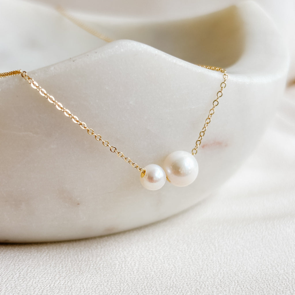 Delicate gold necklace with two pearls on a soft white background