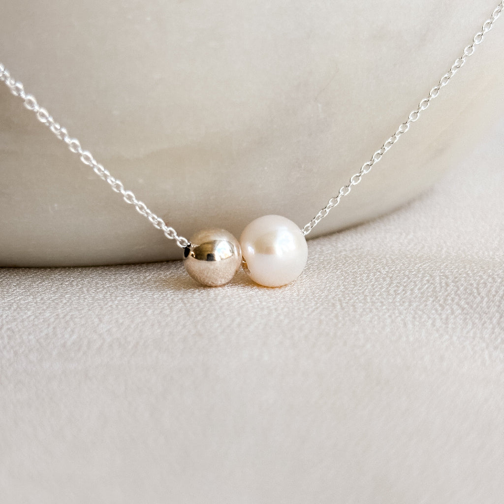 Sterling silver necklace with duo sliding pendants of silver ball bead and pearl on a light background