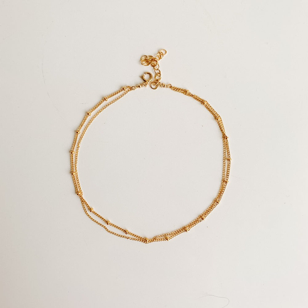 a dainty gold chain anklet featuring a beaded chain and a simple chain with spring ring closure.
