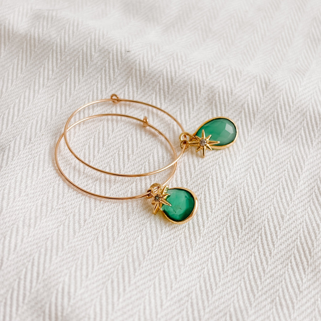 a pair of thin medium sized hoops in 14k gold filled with duo dangly charms; green onyx teardrop-shaped that is bezel set and a tiny North Star with central cz stone that sits in front of the gemstone charm.