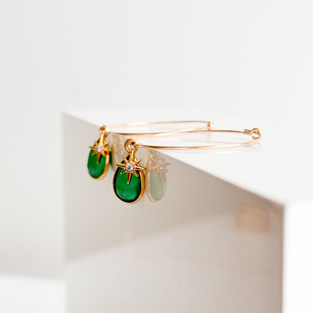 a pair of gemstone hoop earrings in 14k gold filled. The hoops are thin and 30mm featuring a tiny north star charm placed in front of a teardrop-shaped bezel set green onyx charm.