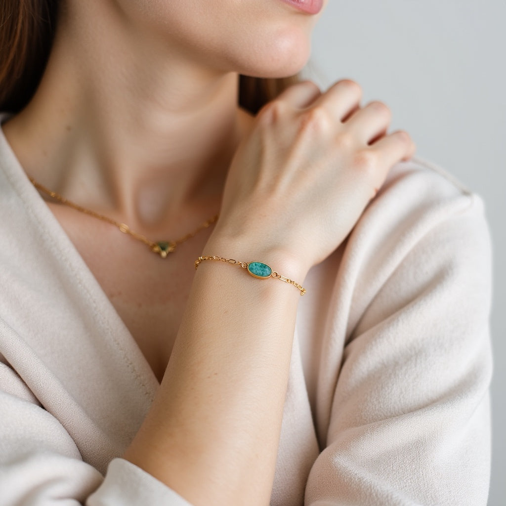 a dainty gold chain bracelet featuring an oval gold framed amazonite. The chain links are long and short and the gemstone is blue-green. The bracelet is shown on a woman's wrist.