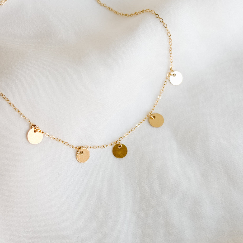 Gold necklace with 5 round pendants that dangle from simple cable chain on a light background