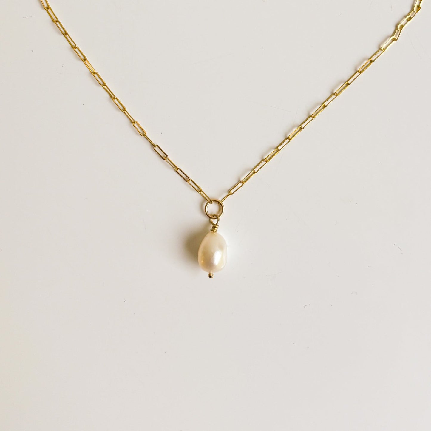 a gold filled necklace crafted from small paperclip chain joined in the center by an open ring from which is suspended an oval shaped pearl.