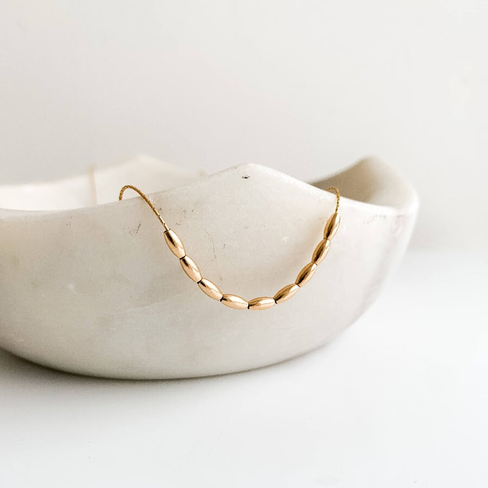 ainty gold necklace featuring 9 petite oval-shaped beads on delicate chain.
