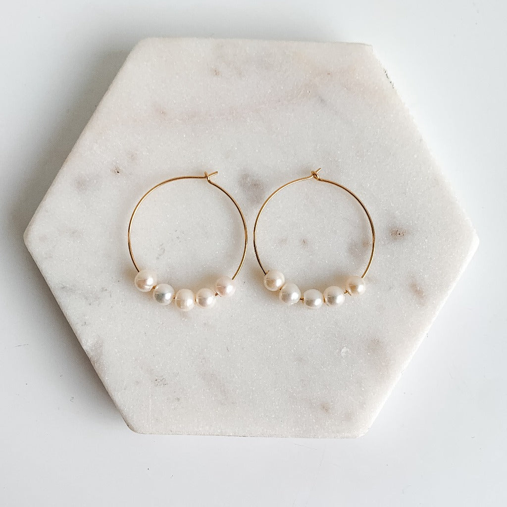a pair of gold hoop earrings with 5 freshwater pearls strung on the wire.