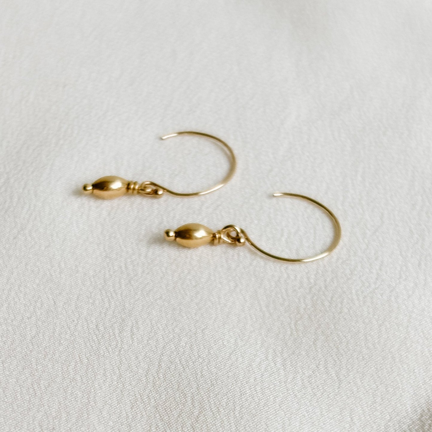 a dainty pair of 14k gold filled circle ear wire earrings that feature a dangling mini oval gold bead charm.