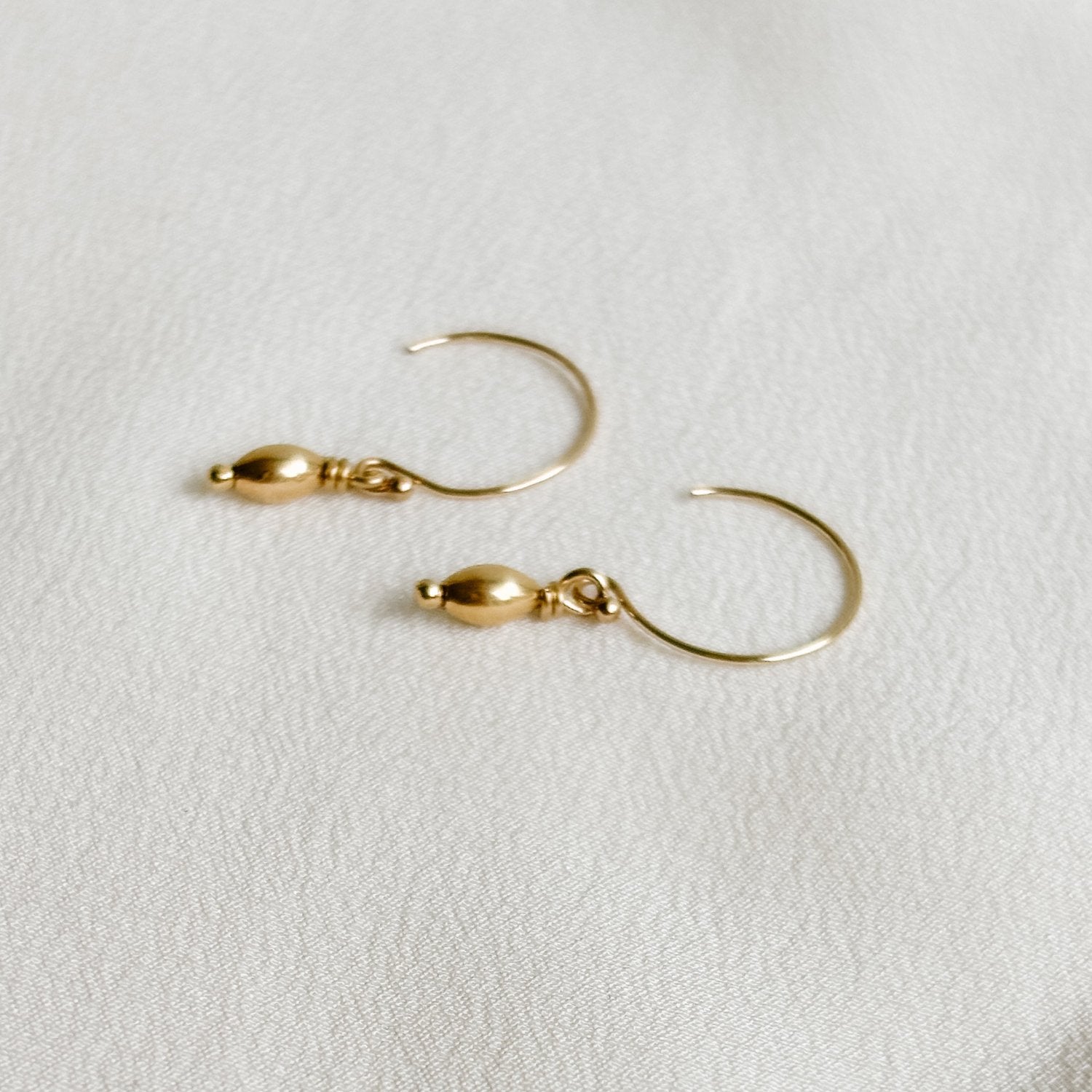 a dainty pair of 14k gold filled circle ear wire earrings that feature a dangling mini oval gold bead charm.
