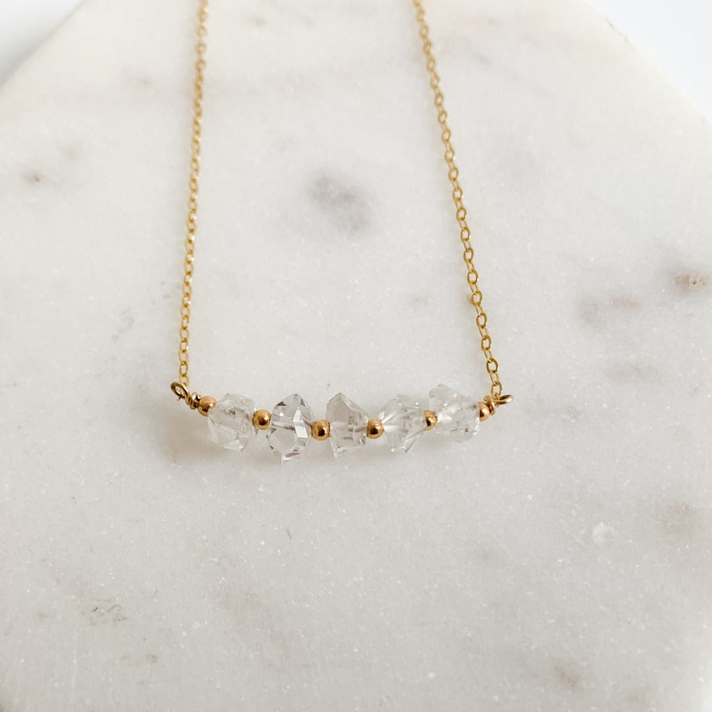 A dainty 14k gold filled necklace with 5 clear Herkimer Diamond crystals set in delicate gold chain. The raw crystals are separated by tiny gold beads.