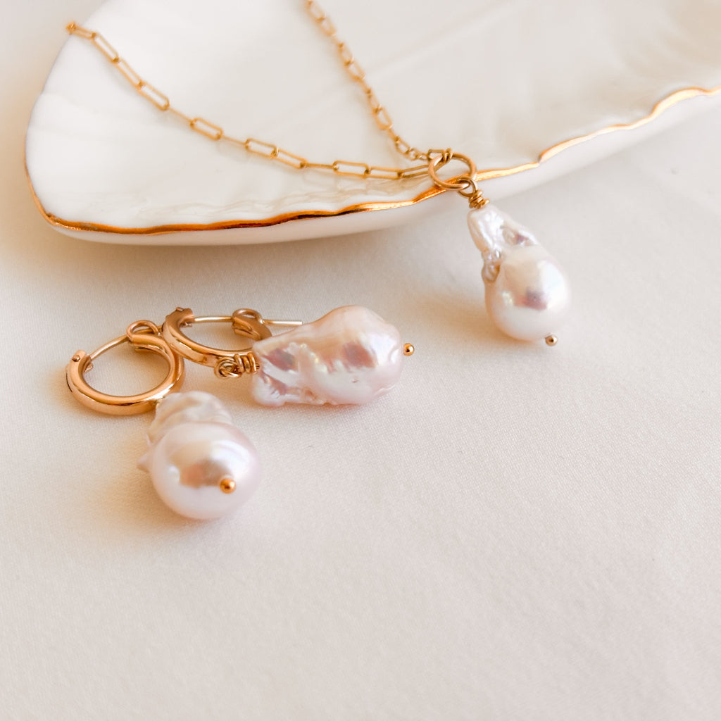 a set of large baroque fireball pearl earrings and necklace. The earrings are 14k gold filled hoops with dangling pearls and the necklace is 14k gold filled paperclip chain with a central ring from which the pearl dangles.
