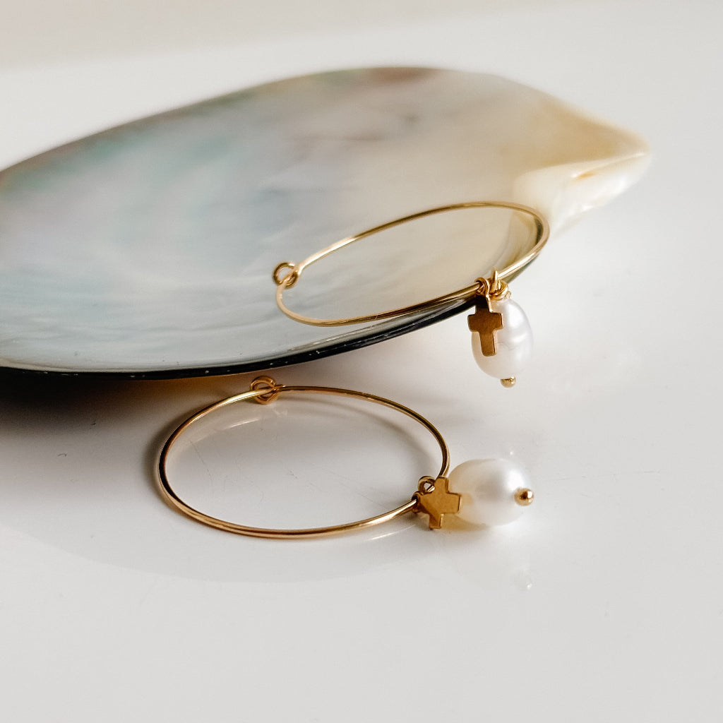 Gold hoop earrings with pearl and cross charms on a white surface