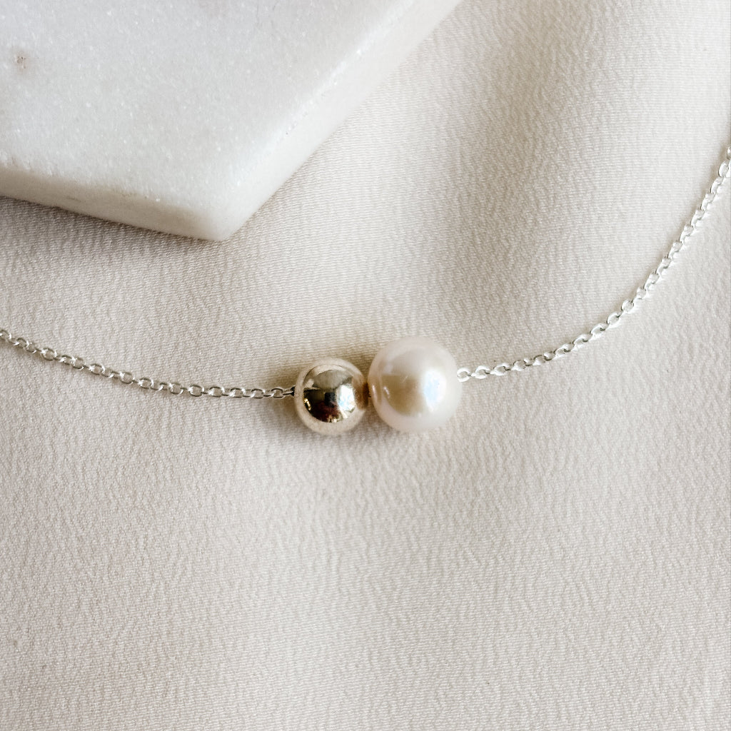 Delicate sterling silver necklace with a single pearl and sterling silver bead on a light background