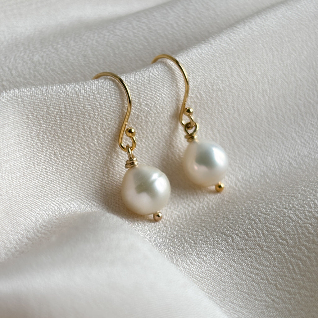 Baroque pear shaped pearl earrings on a soft white fabric background