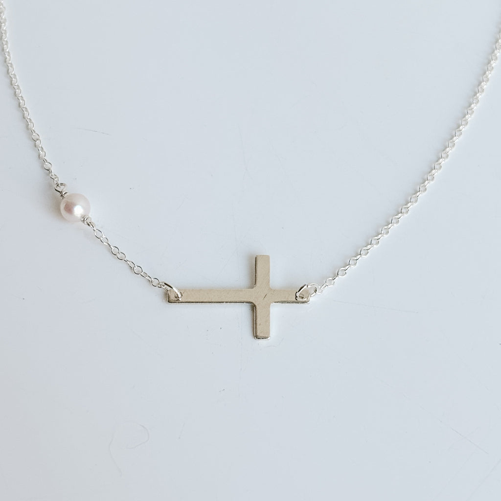 Silver sideways cross necklace with a pearl on a light gray background