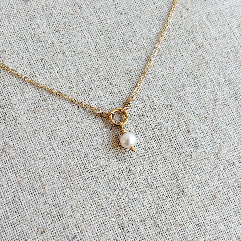 14k gold filled necklace with a single tiny pearl pendant on a textured beige fabric background