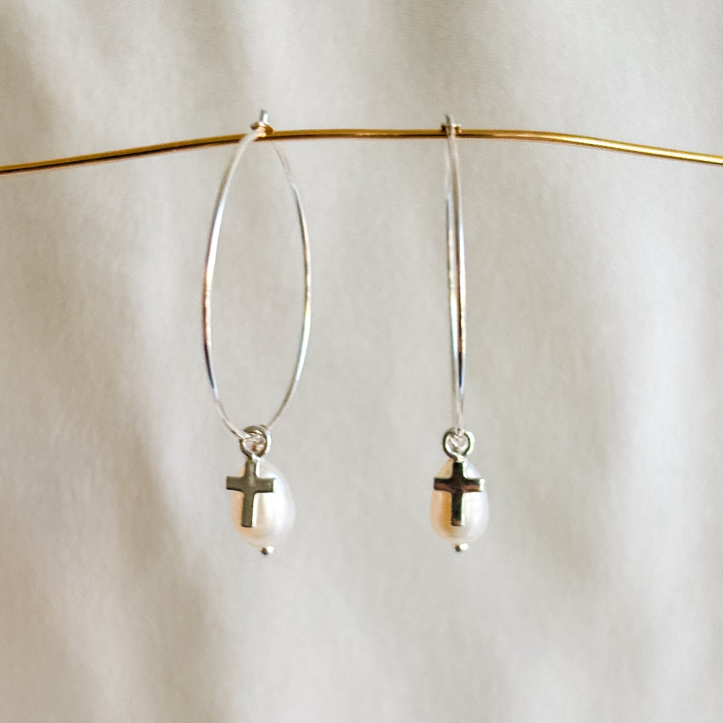 Sterling silver hoop earrings with pearl and cross charms on a white background