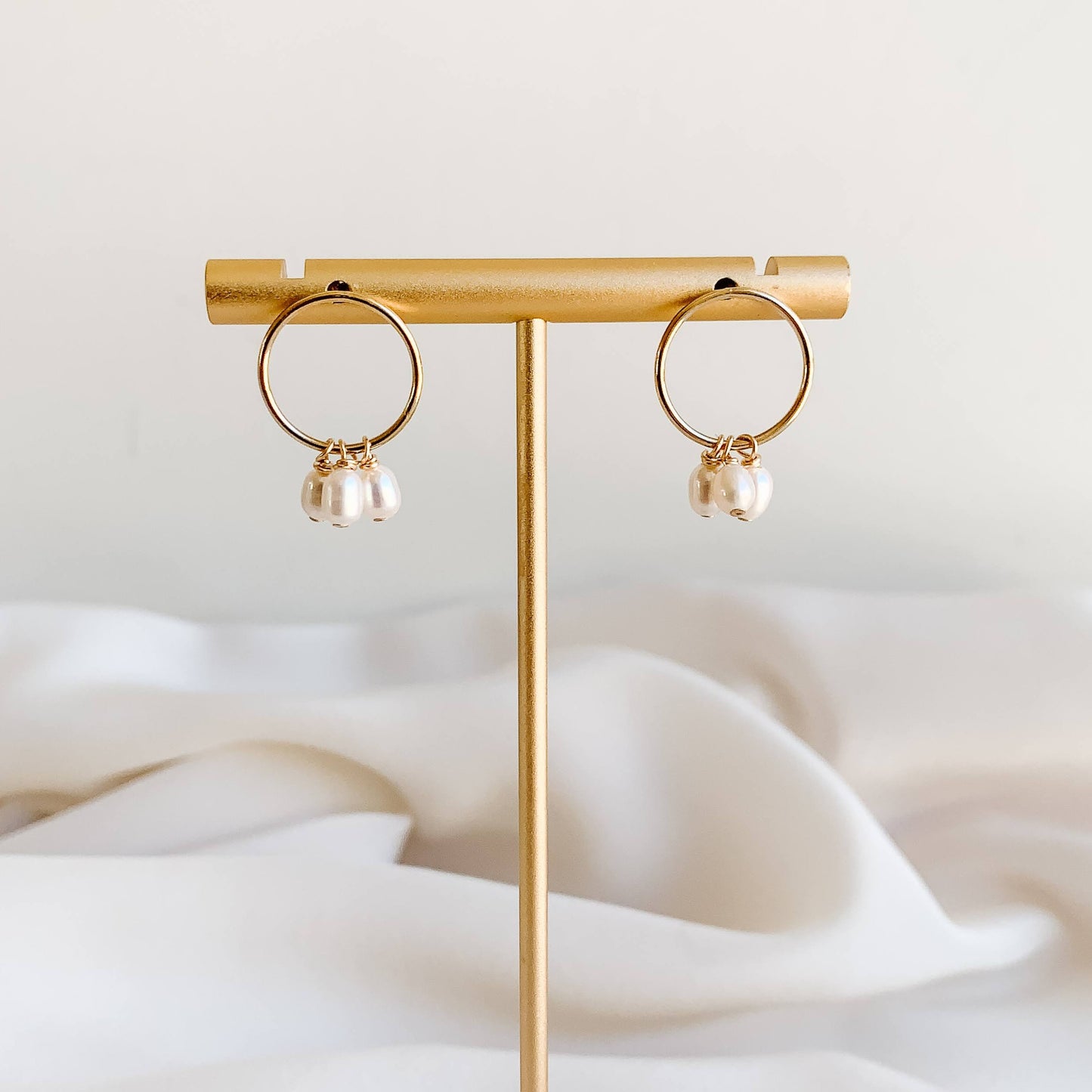 Dainty pearl drop earrings in 14k gold filled. The modern front-facing open circle hoop studs feature a trio of petite freshwater pearl drops.