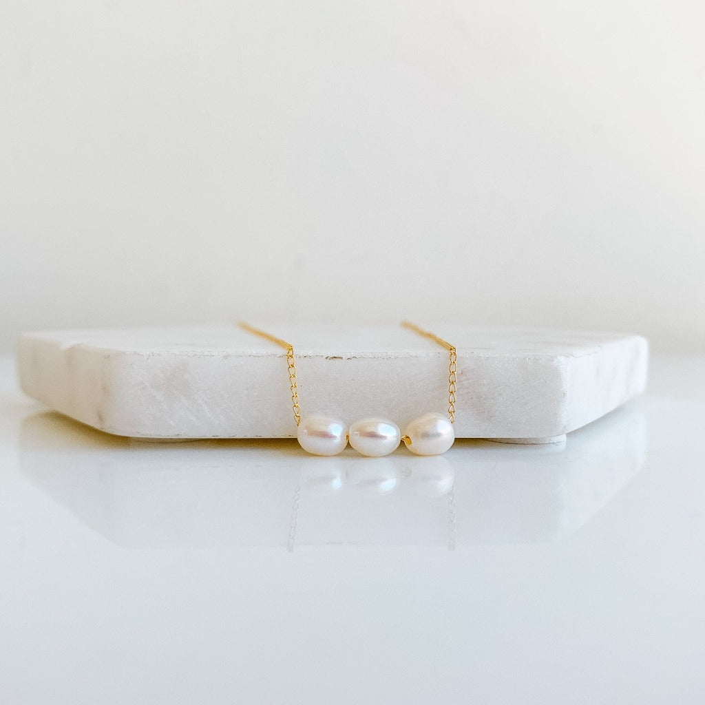 A dainty freshwater pearl necklace featuring three high luster oval pearls strung on simple gold chain.
