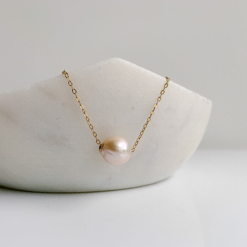 A gold filled chain necklace that features a single baroque pearl that "floats" or slides along the chain. The pearl is a genuine Edison pearl with high sheen and some wrinkling.