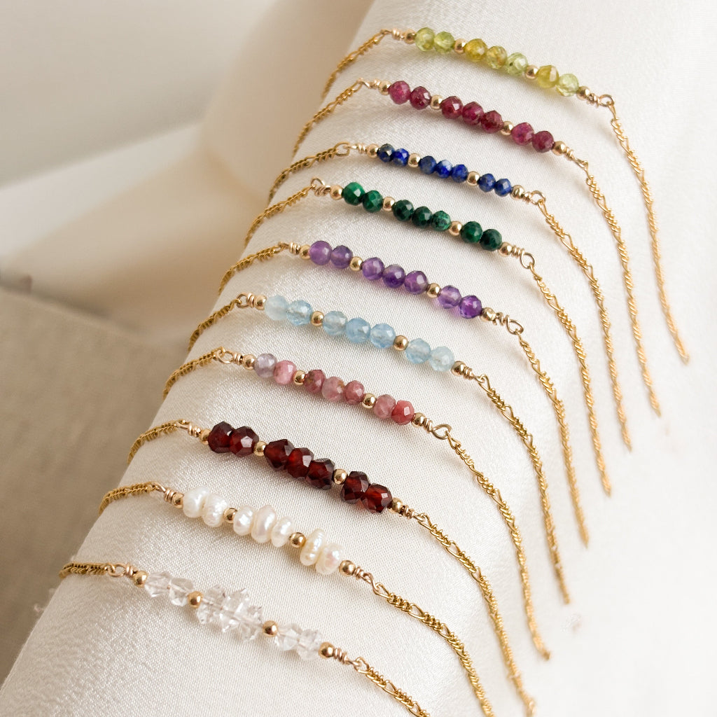gold gemstone bracelets in all the birthstones of the year shown on a light background.