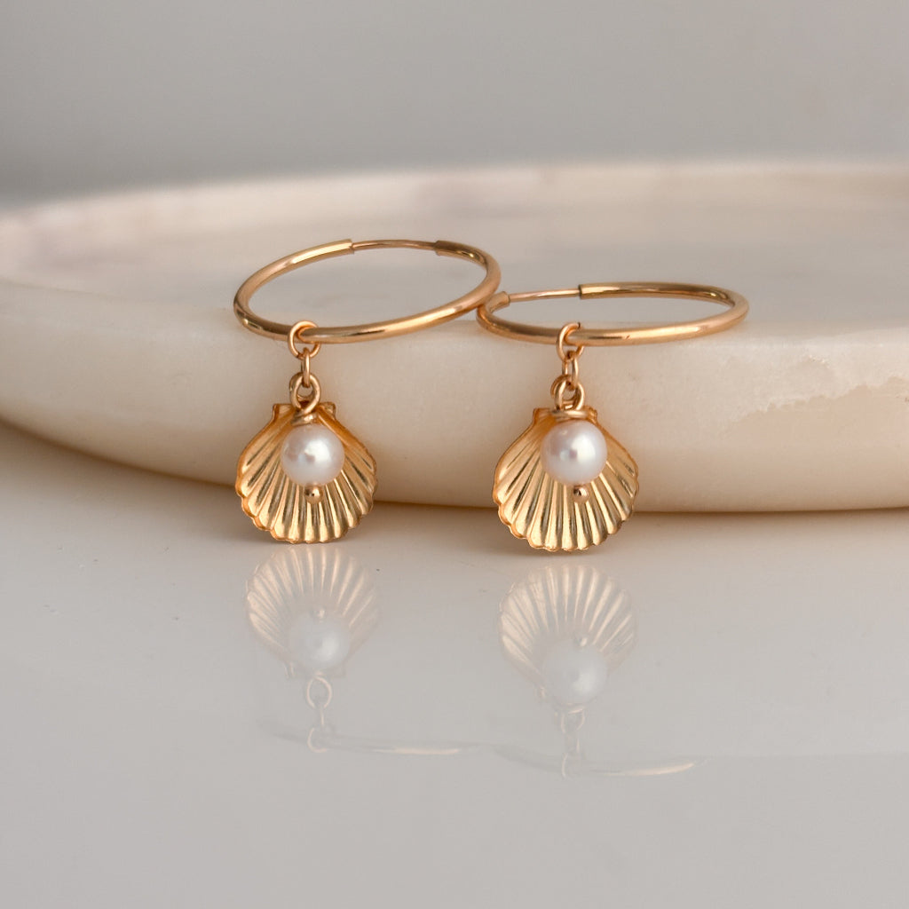 Gold earrings with shell-shaped pendants on a light background