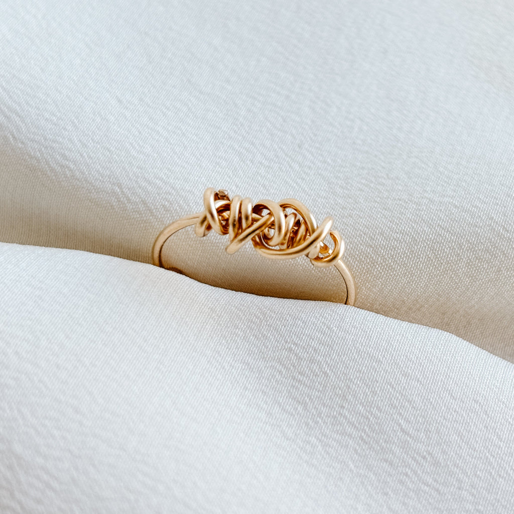 a 14k gold filled knot ring on a soft white fabric background