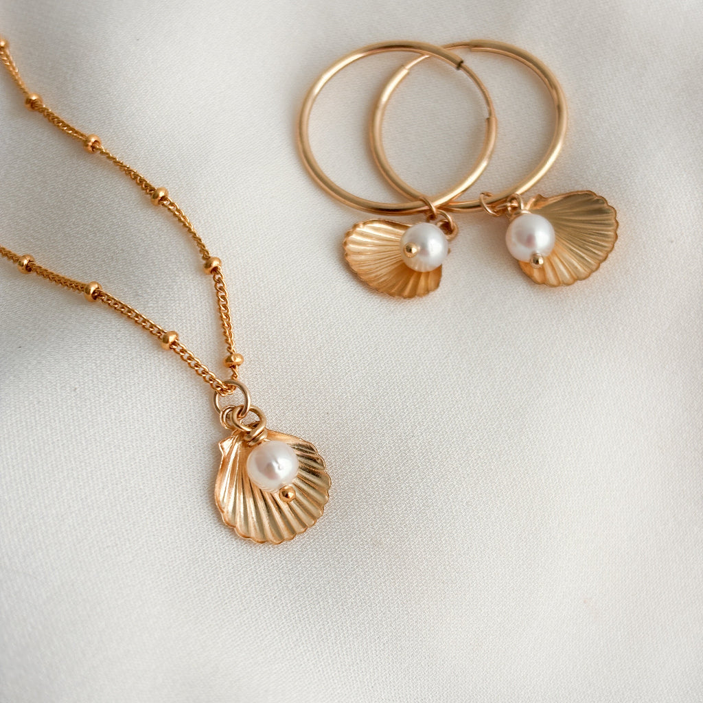 Gold necklace and earrings with shell and pearl details on a light background