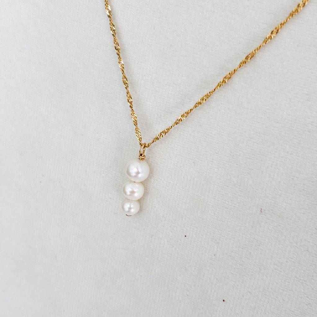 Gold necklace with a three pearls pendant on a light gray background
