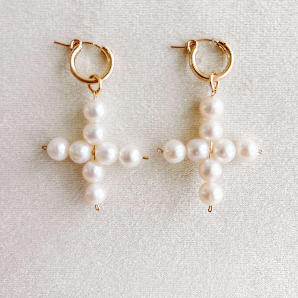 Pair of pearl cross-shaped hoop earrings on a light gray background