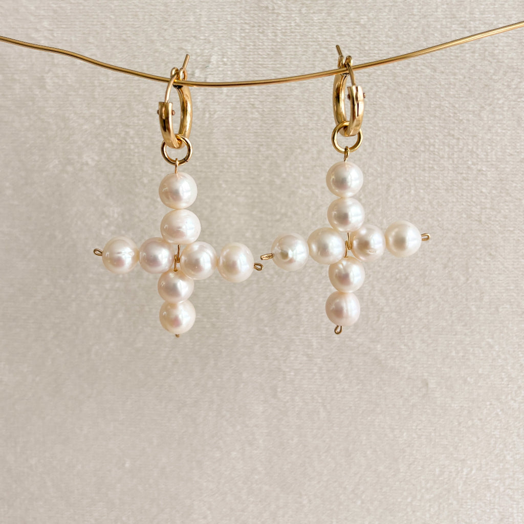 Pearl cross-shaped earrings on a light background